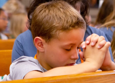 Preteen boy praying in a pew.