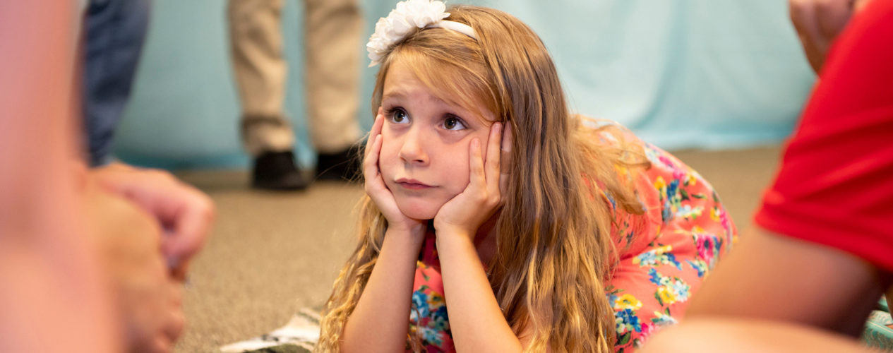Elementary aged girl is resting her chin on her hands as she leans forward on the ground.