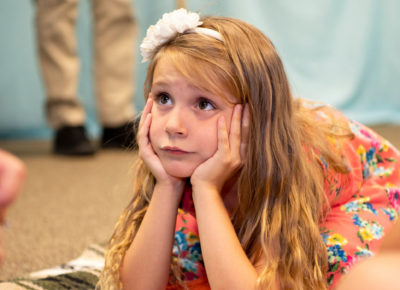 Elementary aged girl is resting her chin on her hands as she leans forward on the ground.