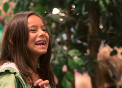 A elementary-aged girl is laughing as she recoils from tossing a ping-pong snowball into a wreath off screen.