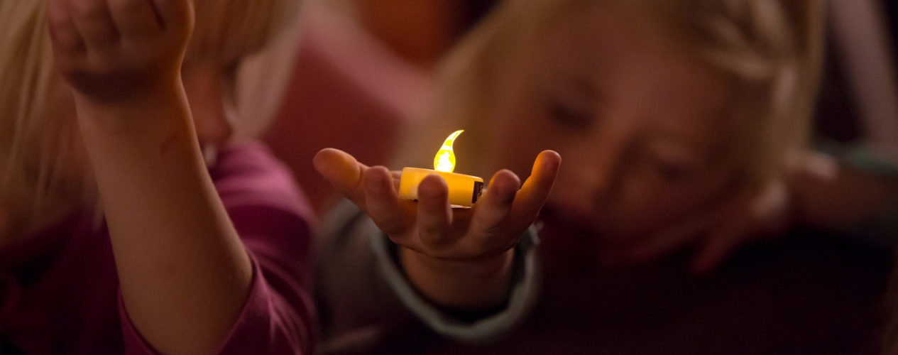 An elementary girl holding a tea candle light on her palm.