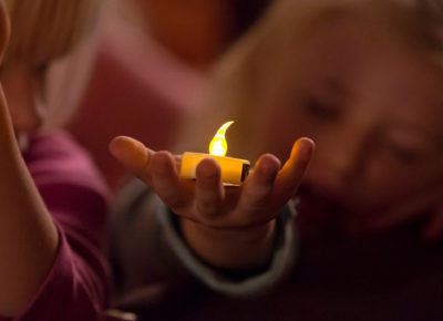 An elementary girl holding a tea candle light on her palm.