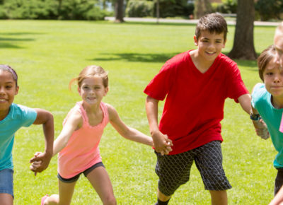 A group of elementary and preteen children running around playing ultimate keepaway tag outside.