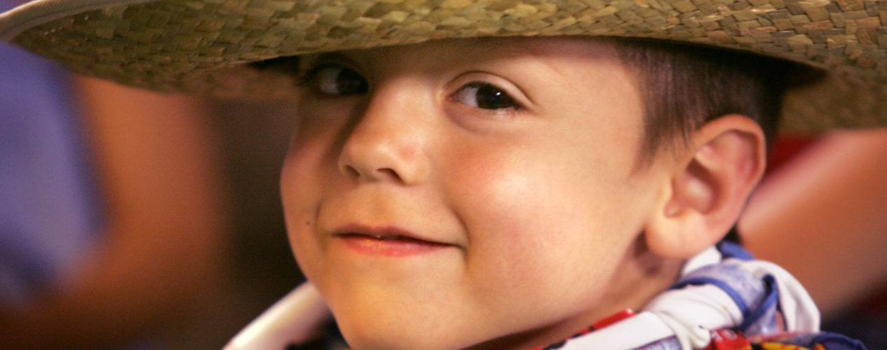 An elementary boy with a small smirk is wearing a cowboy hat and a bandana around his neck.