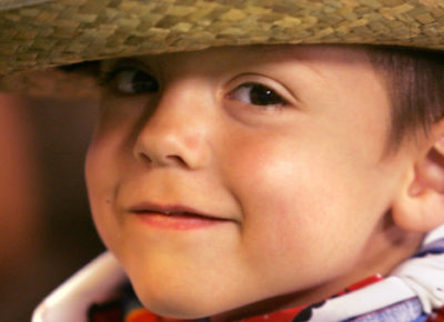 An elementary boy with a small smirk is wearing a cowboy hat and a bandana around his neck.