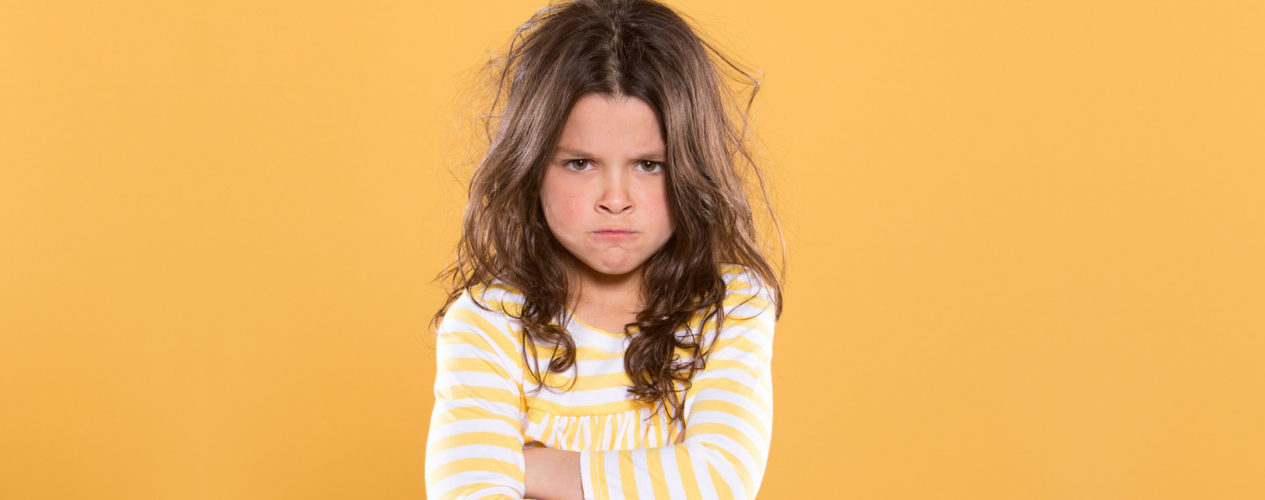 Elementary-aged girl with messy hair, arms crossed, and a pouty face.