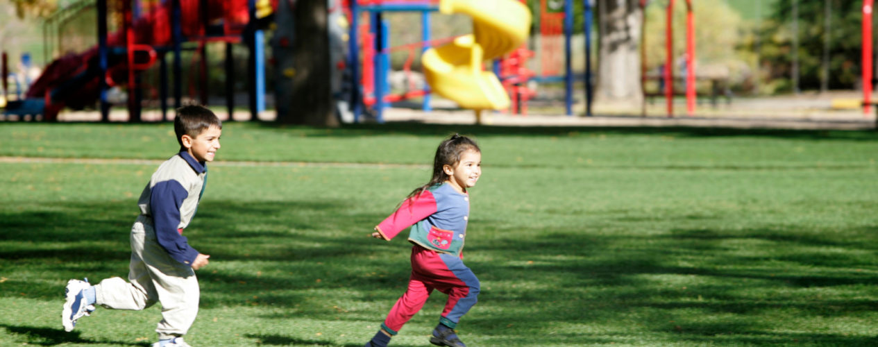 Two children running in front of an outdoor playspace.