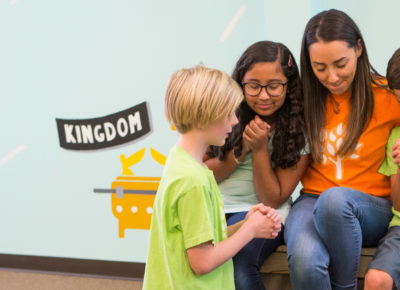 A female volunteer prays with three preteen kids on the National Day of Prayer.