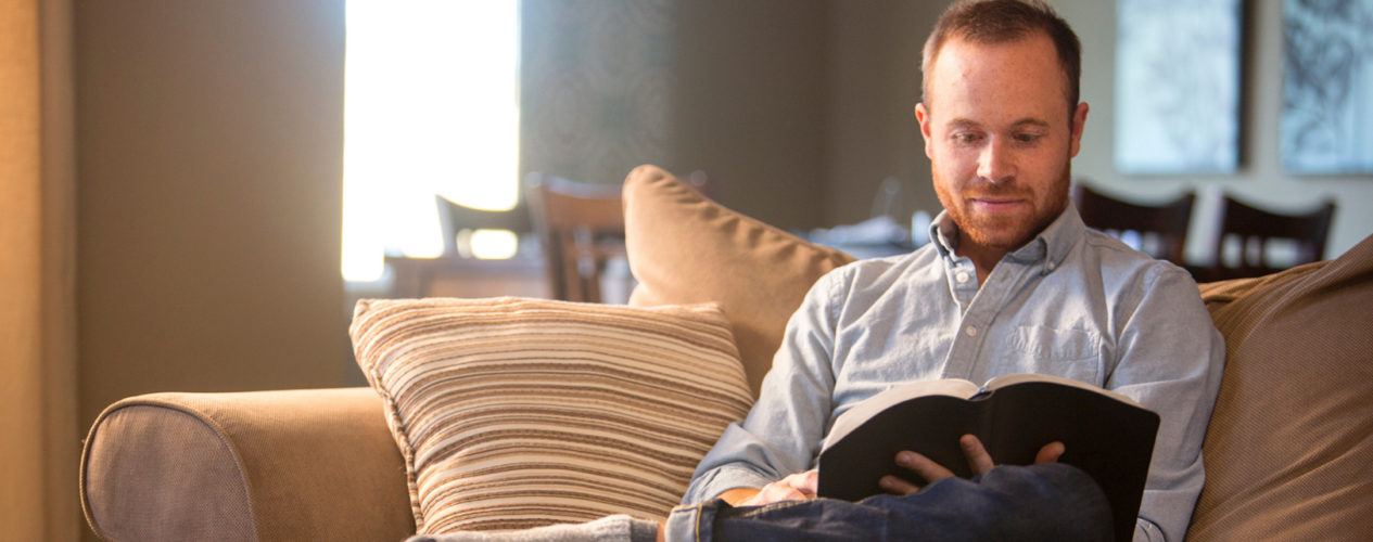 Male children's ministry sitting on his couch while he reads the Bible.