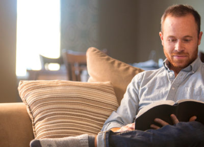 Male children's ministry sitting on his couch while he reads the Bible.