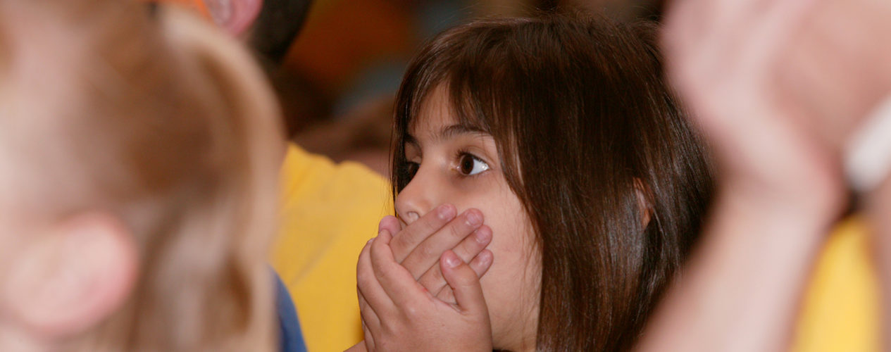 An elementary girl covers her mouth with her hands.