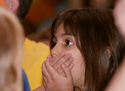 An elementary girl covers her mouth with her hands.