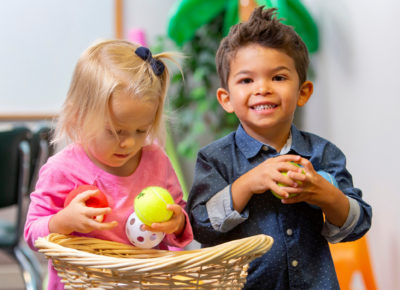 Two toddlers in the church nursery are grabbing toys out of a basket.