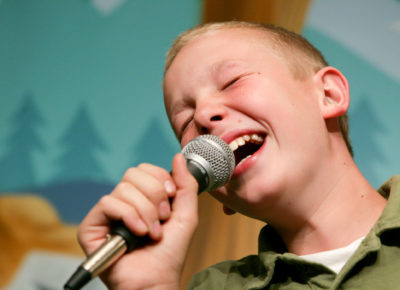 A boy single Christmas carols into a microphone.