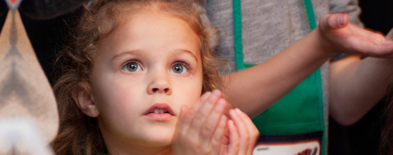 A young elementary girl stares in wonder as she cups her hands.