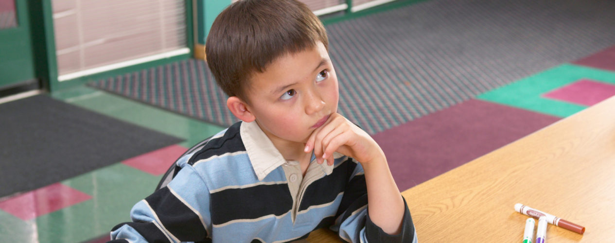 An elementary-aged boy rests his chin on his hand as he ponders something.