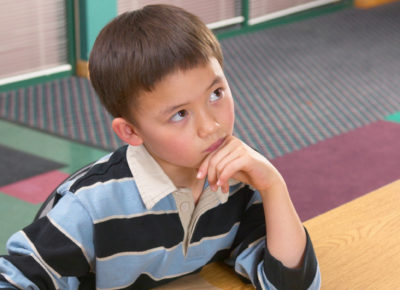 An elementary-aged boy rests his chin on his hand as he ponders something.