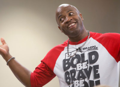 A grown man is giving a goofy expression with his hands up in the arm and his shoulders shrugging.