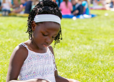 An elementary-aged girl sits outside on the grass reading her Bible.