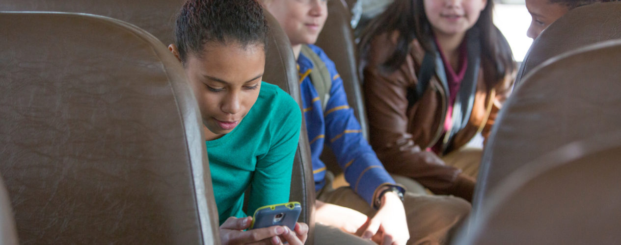 A preteen girl sitting on a bus looking at her phone. She is a victim of cyber bullying.