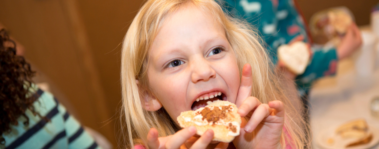 Elementary aged girl eating a piece of bread with cinnamon and sugar on top.