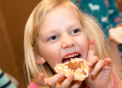 Elementary aged girl eating a piece of bread with cinnamon and sugar on top.