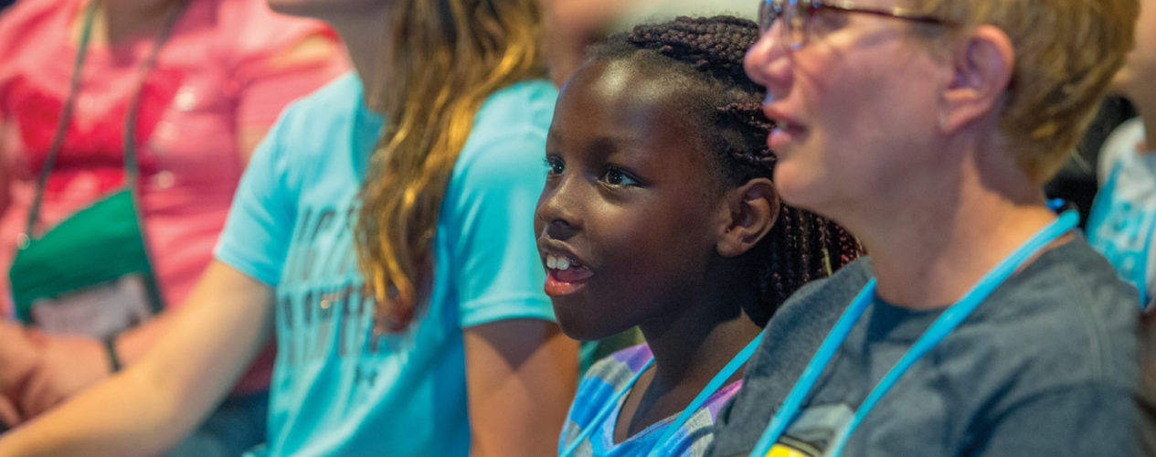 A preteen girl sits in her children's ministry large group session with a look of wonder on her face.