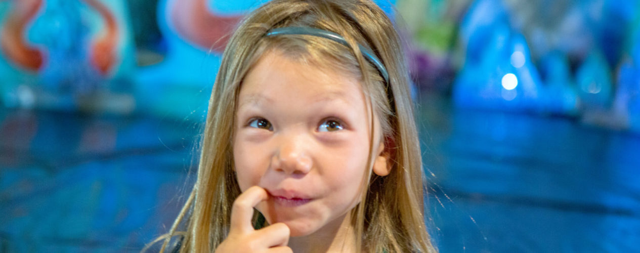 An elementary-aged girl sticks her finger in her mouth as she thinks about the manners lesson.