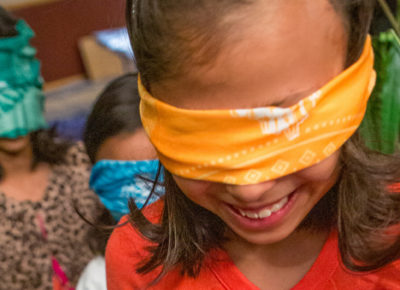 An elementary girl with a blindfold on smiles as she participates in an obstacle course.