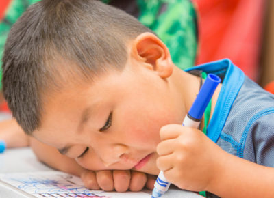 A preschool boy is sadly coloring with a marker. He's working through some grief.