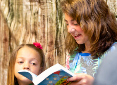 An older elementary girl reading aloud from the Bible to younger kids during a Sunday school lesson.