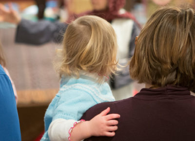 A mom holding her toddler aged girl at a family ministry event.