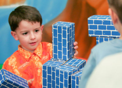 An elementary boy has a look of concentration as he stacks large cardboard building bricks.