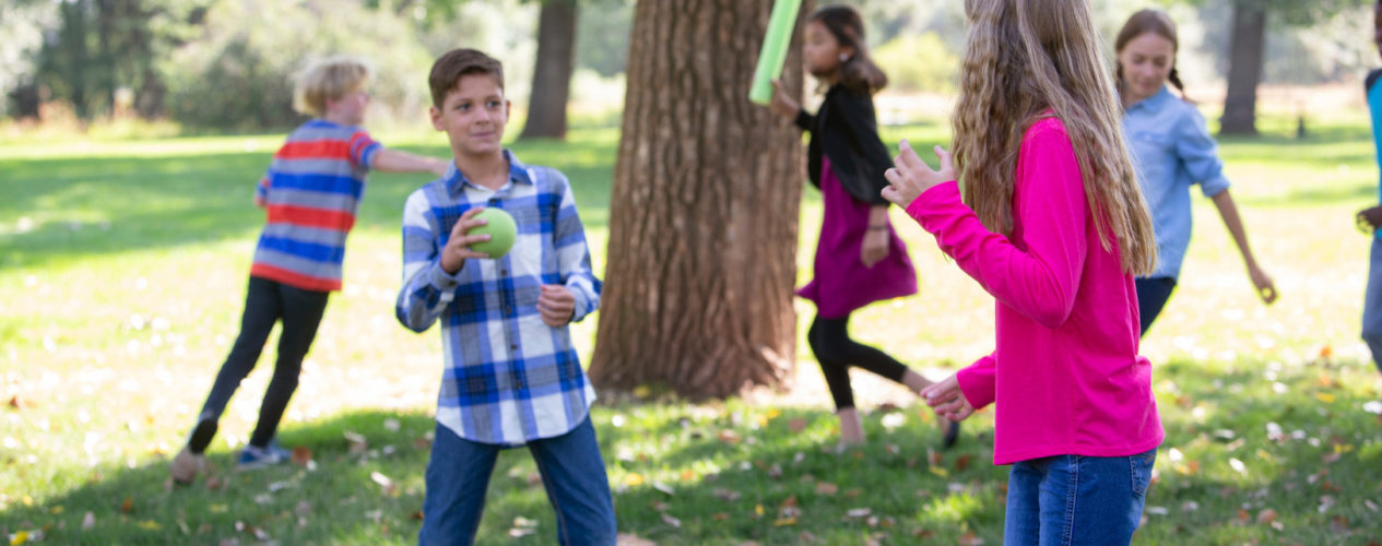A group of preteens are playing a game at a park during the fall.