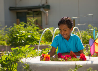An elementary-aged boy is sitting in a garden on Earth Day.