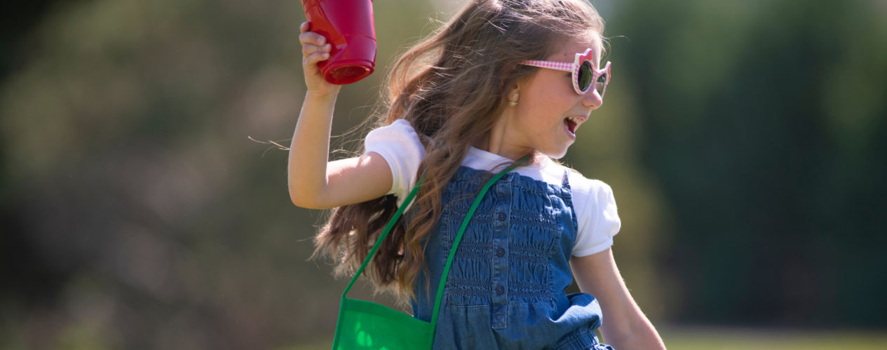 An elementary aged girl in overalls and sunglasses frolics outside during the summer.
