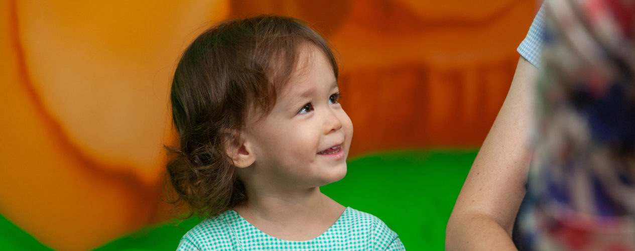 An toddler smiles up at an adult.