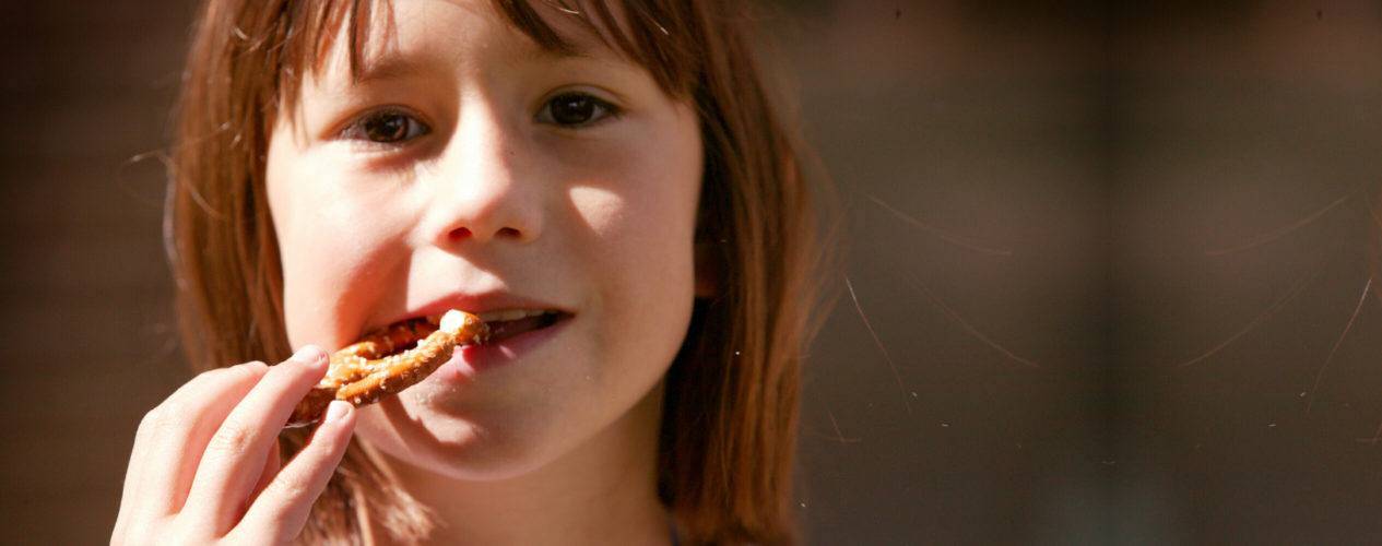 An elementary aged girl is eating a twisted pretzel.