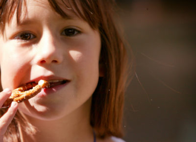 An elementary aged girl is eating a twisted pretzel.