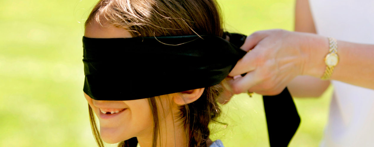 A preteen girl smiles as a blindfold is placed over her eyes.