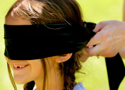 A preteen girl smiles as a blindfold is placed over her eyes.