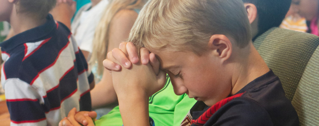 A preteen boy is praying at a prayer station.