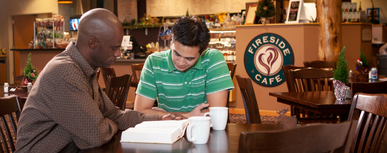 Two men reading a Bible together in a coffee shop.