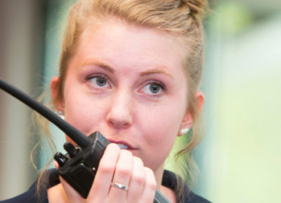 A woman volunteer holding a walkie talkie to her mouth. Her expression is very serious.