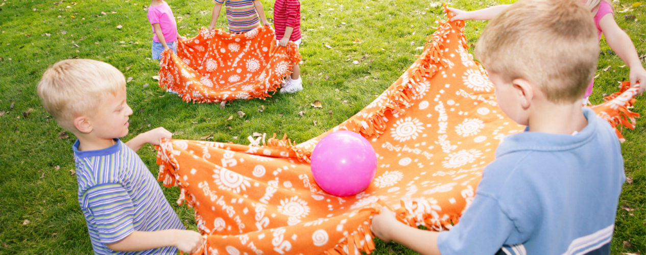 A group of children holding two blankets are playing blanket volleyball.