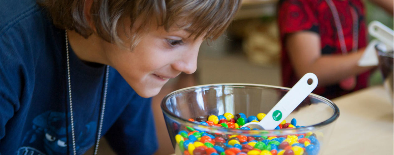 Preteen boy looks wide-eyed at a big bowl of color candies.