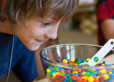 Preteen boy looks wide-eyed at a big bowl of color candies.