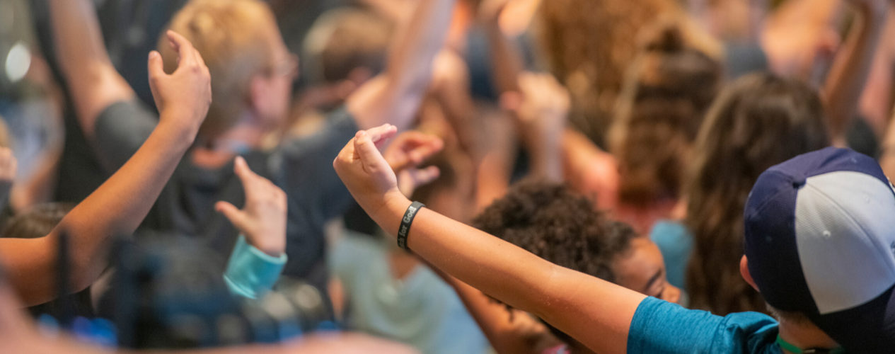A group of children and volunteers raise their hands in worship during a lesson on the Pentecost and Holy Spirt.