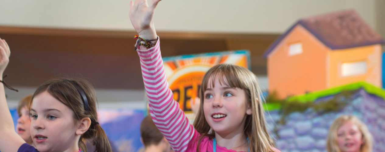 An elementary girl raises her hand during a children's message.
