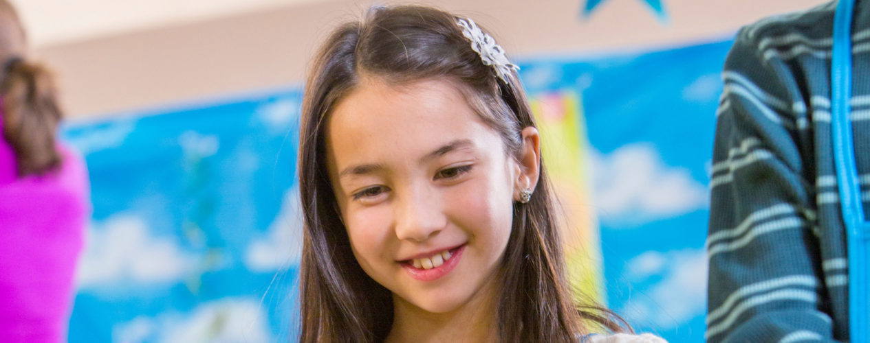 An older elementary girl smiles as she listens to a message.